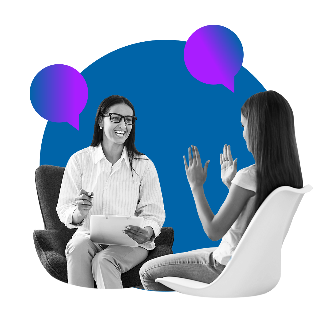 Two people seated in conversation, one smiling while holding a tablet and pen as the other gestures with both hands
